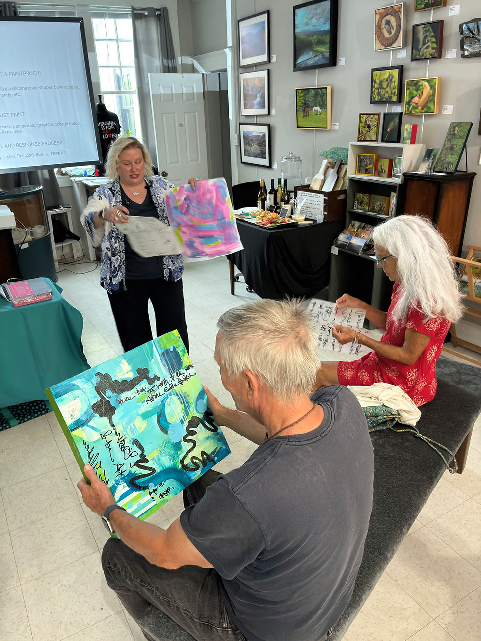 Precious Burger is in the background holding collage fodder while two guests at VECCA look at a work of art up close and some of her other collage fodder.