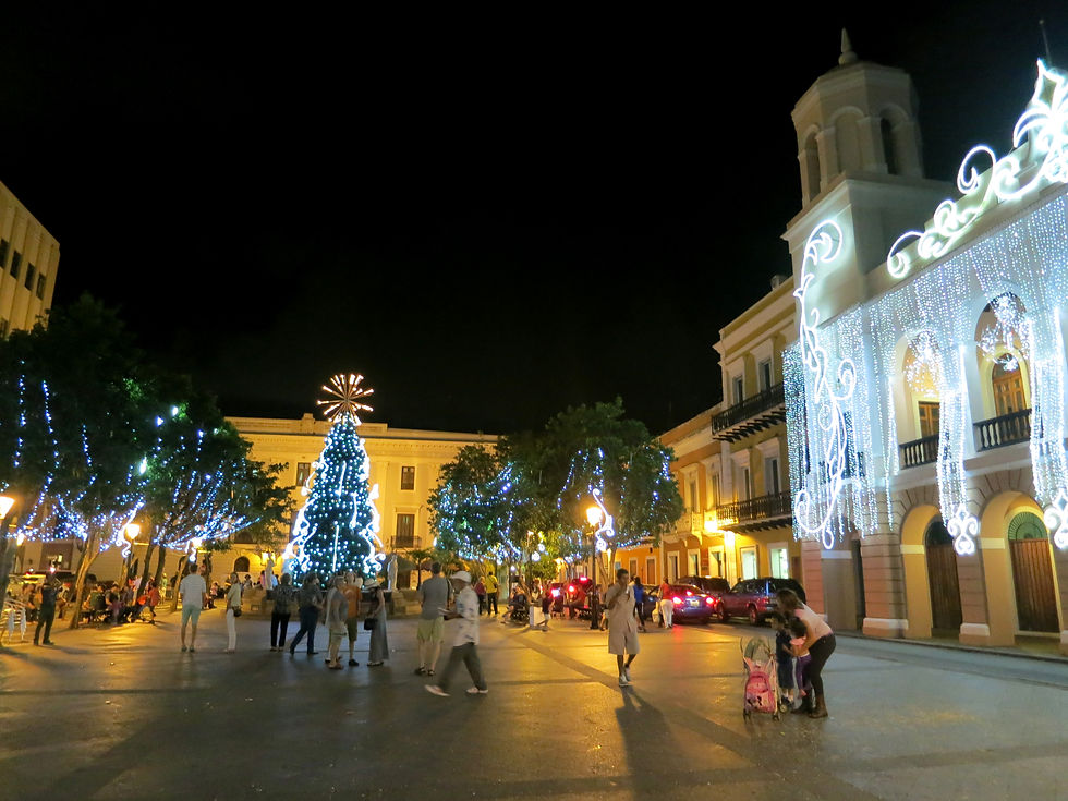 Festive street at night with people strolling, a large lit Christmas tree, and buildings adorned with glowing lights, creating a joyful mood.