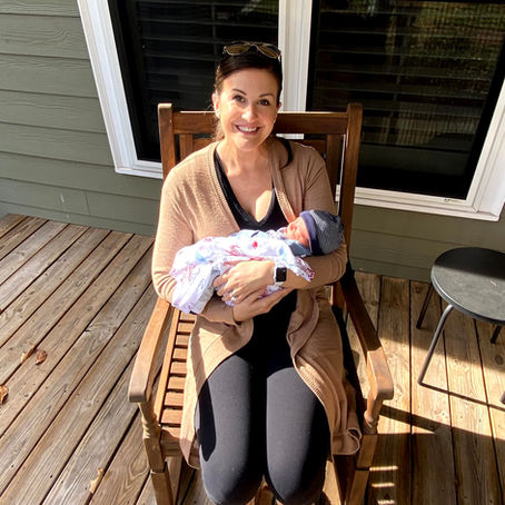 New mom holding her swaddled newborn on the front porch after bringing baby home from the hospital