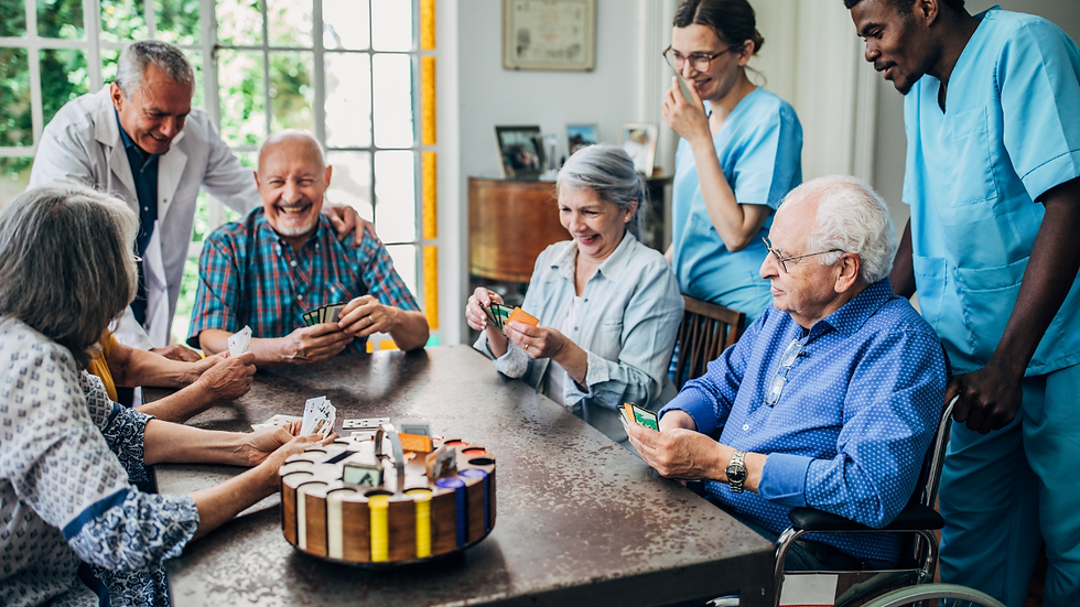 Multicultural aged care workers smiling and chatting with elderly clients in a relaxed group setting in Australia.