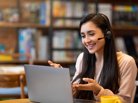 Smiling young woman in headset having an online English conversation lesson on her laptop in a relaxed learning space.