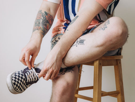 Man tying up his shop lace with tattoos on his legs
