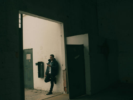 man leaning against a wall in a dark corridor holding his phone