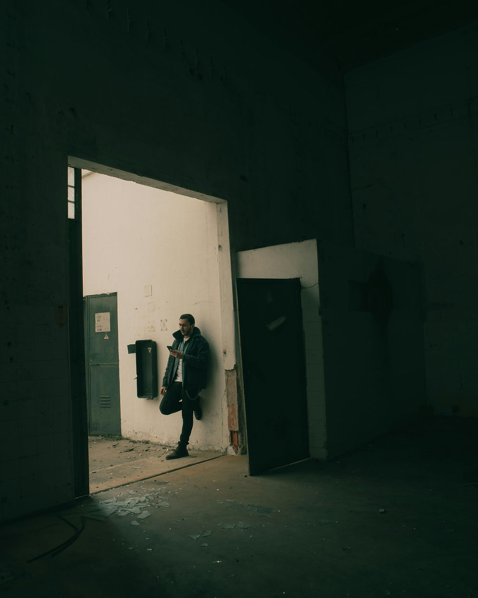 man leaning against a wall in a dark corridor holding his phone