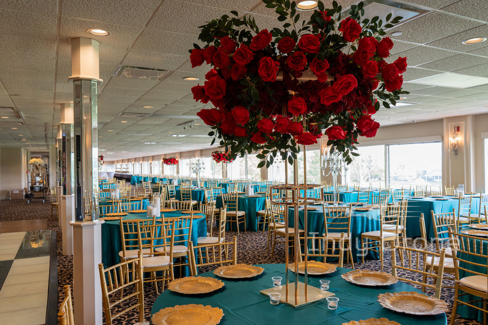 Reception hall setup with round banquet tables, linens, and tall floral arrangements
