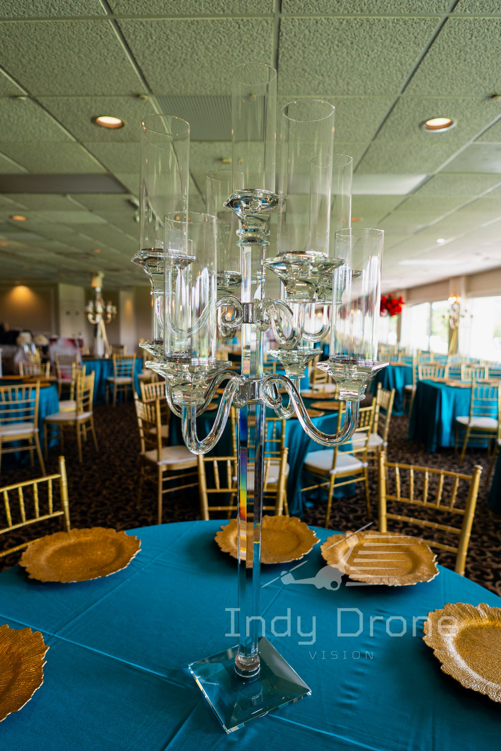Reception hall setup with round banquet tables, linens, and tall floral arrangements