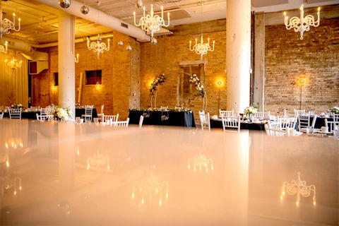 Elegant ballroom with shiny dance floor, brick walls, chandeliers, and event tables.