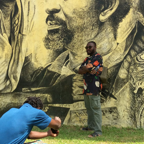 Visitor beside a portrait mural at Nkyimkyim Museum in Ada