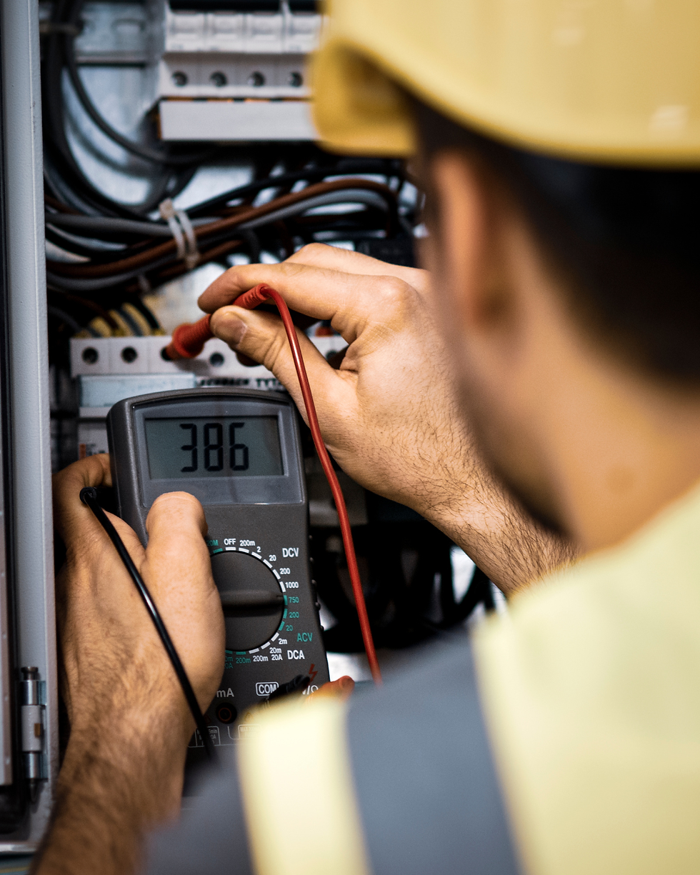 Electrician uses a multimeter, with the number 386 visible, to test electrical panel