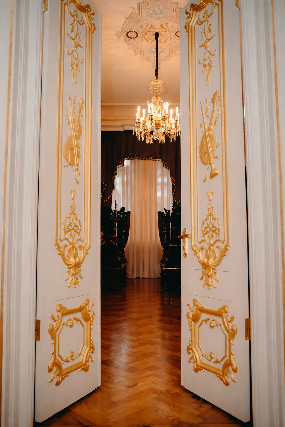 Ornate gold leaf gilded double doors with handcrafted baroque detailing and chandelier interior in Ajman luxury residence.