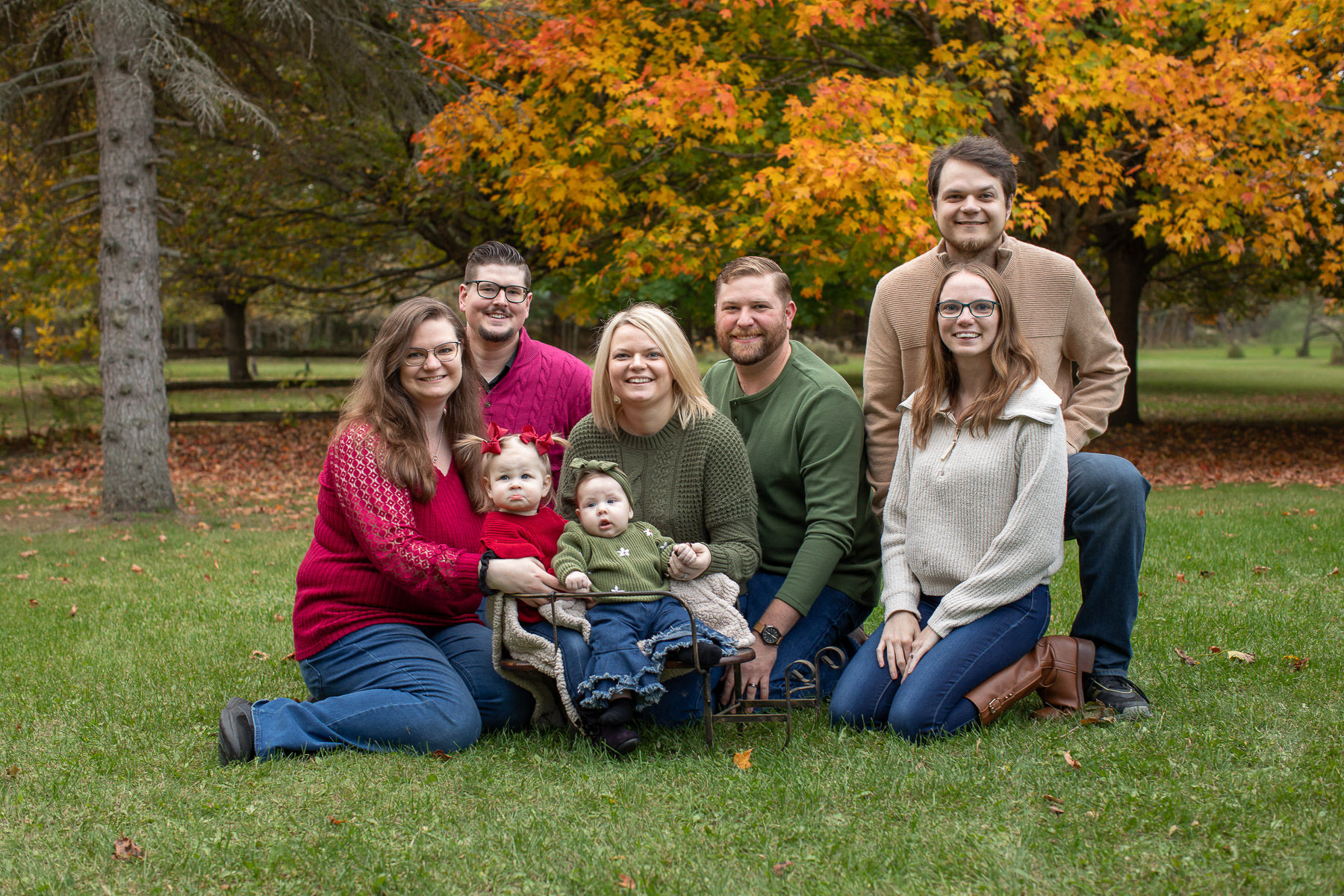 Extended family seated together outdoors beneath colorful fall trees for family portraits in Ubly, Michigan.