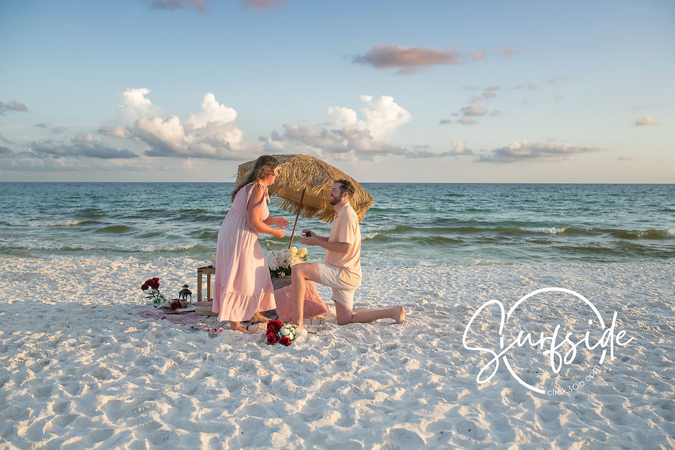 surprise proposal in 30A at Seagrove Beach, groom kneels at golden hour while waves glow and a romantic picnic set-up for two waits behind them