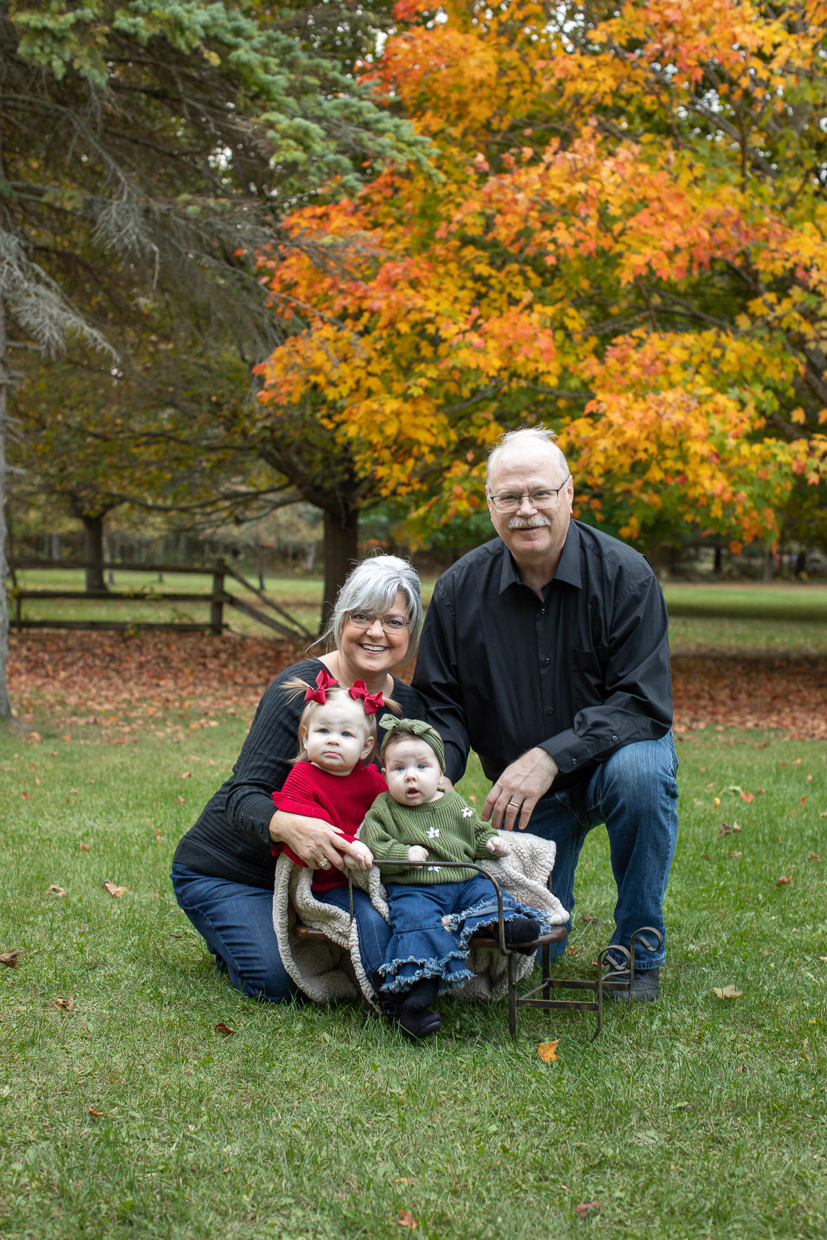 Grandparents posing with their granddaughter in a red sweater during extended family fall portraits in Ubly, Michigan.