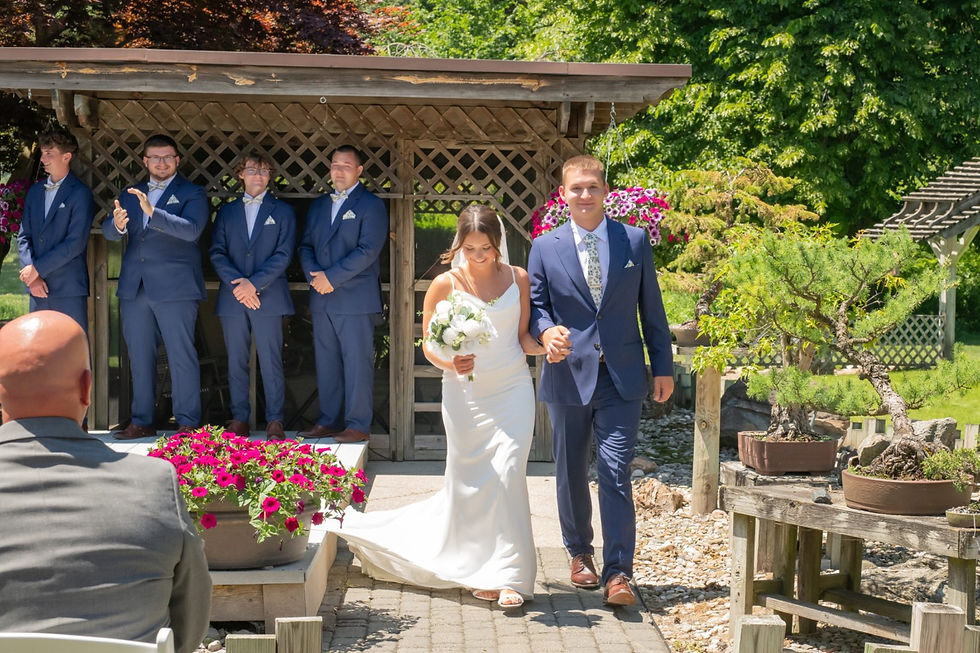 Newly married couple walking hand in hand down the aisle after their outdoor wedding ceremony in Port Austin, Michigan, with their wedding party celebrating behind them.