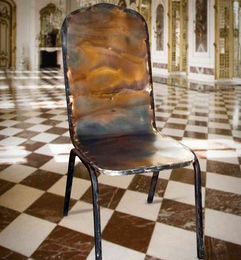 Metal chair with unique rust coloured patterns in a room with a checkered floor, Ferric Garden.