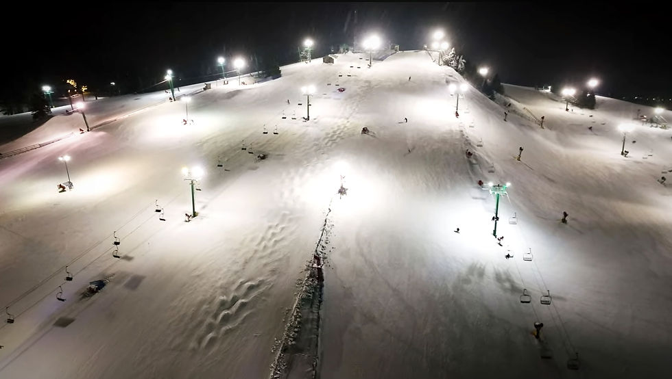 Nighttime ski slope with skiers descending under bright lights. Snowy terrain, chairlifts, and trees visible. Calm, serene atmosphere. trailblaze detroit expedition detroit detroit's ski hills resorts skiing metro adventure series visit tourism michigan pine knob resort clarkston