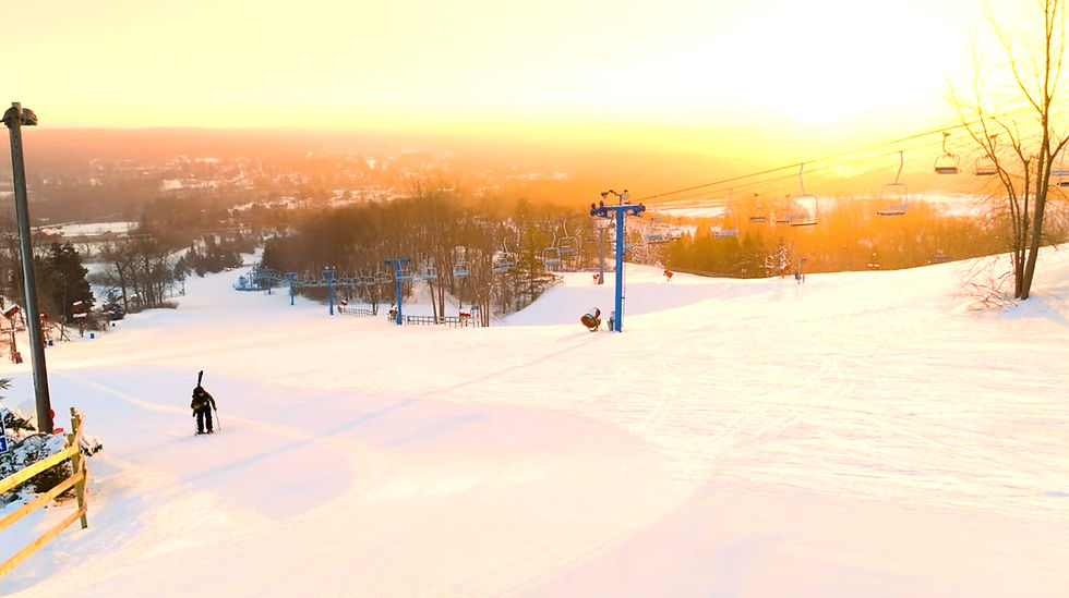 Skier carrying poles on a snowy slope at sunset with ski lifts in the background. Warm hues create a serene, golden atmosphere. trailblaze detroit expedition detroit detroit's ski hills resorts skiing mt holly metro sunrise adventure series visit tourism dan cooke