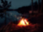 Campfire with glowing embers by a dark lake, surrounded by trees. Sparks fly upward, creating a warm, serene atmosphere in twilight. backpacking near detroit michigan april best month gear trails potawatomi waterloo pinkcney chief pontiac trail state parks recreation areas adventure guided tours expedition detroit