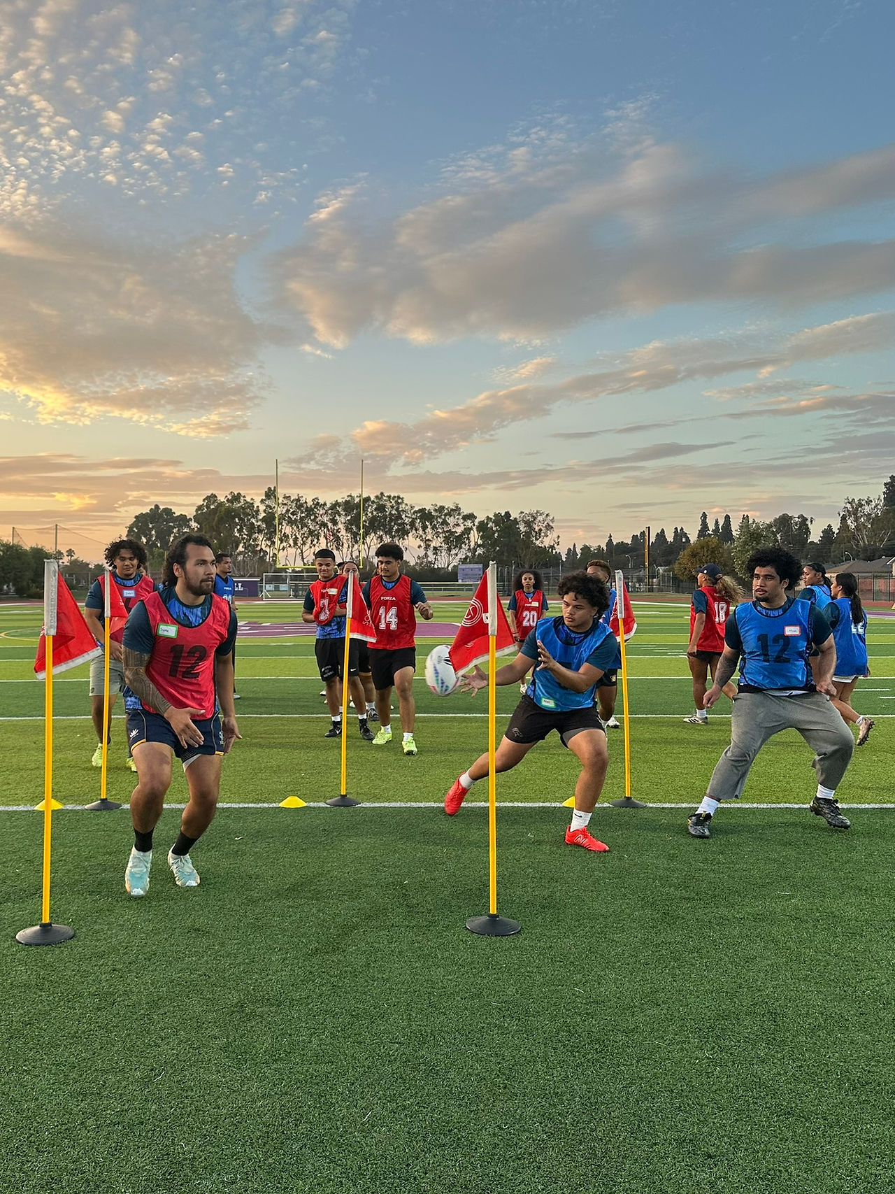 rugby players in red and blue jerseys running a drill in between yellow and red field flags