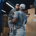 Outside of Logistics Warehouse_ Male Employee Unloading Delivery Truck with Cardboard Boxe