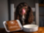 a dog sat in front of a bowl with a packet of the dog food