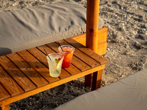 Two refreshing drinks on wooden table Ftelia Beach Bar, sandy beach background.