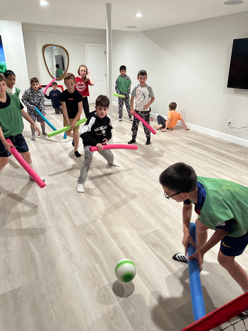 Children playing noodle hockey indoors.