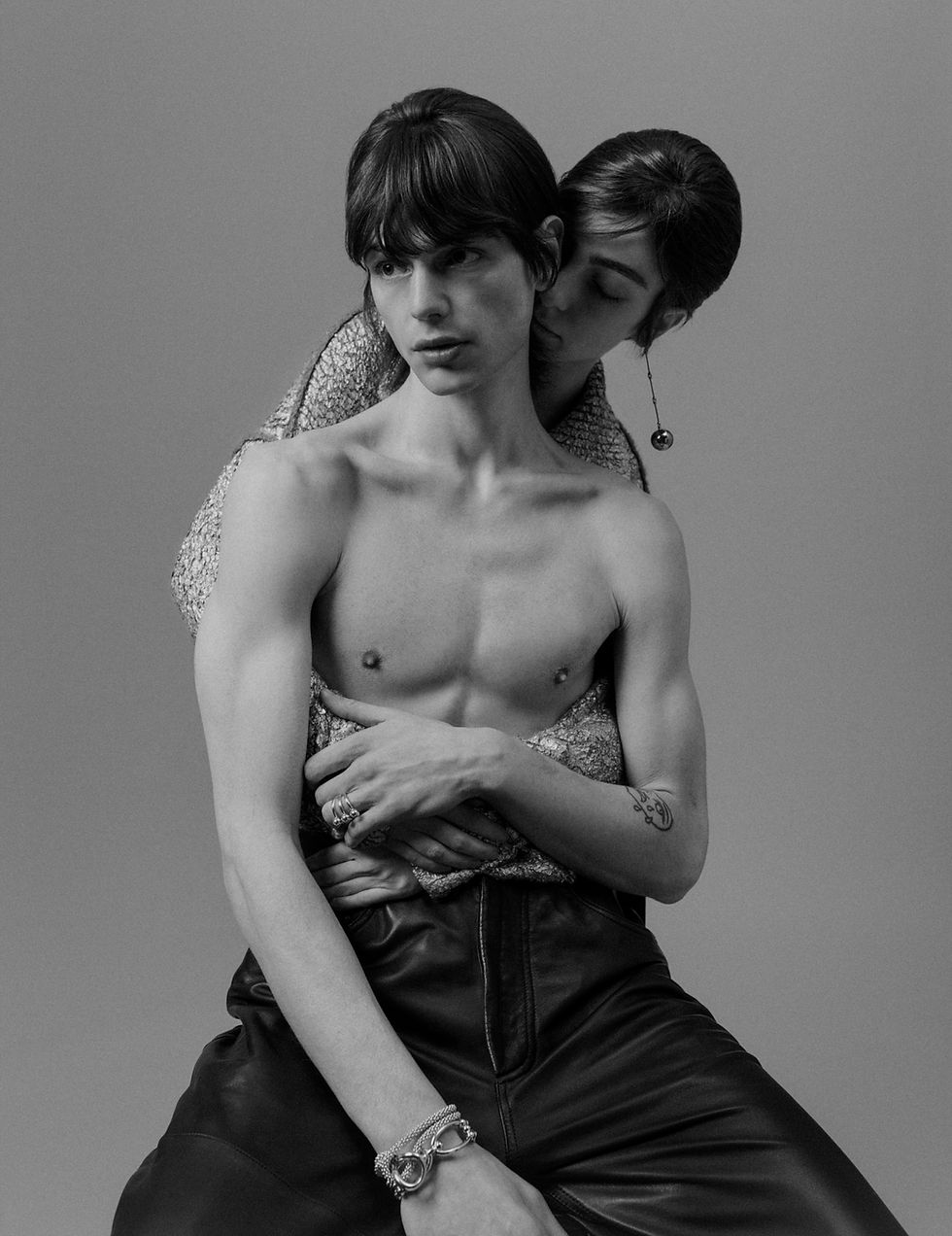 A striking black-and-white photograph of two models in an intimate embrace, blending fashi