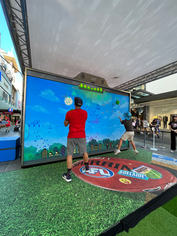 AFL fans playing Space Invaders during the Gather Round at the Rundle Mall AFL Fan-Zone