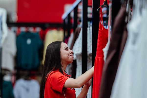 Woman in red shirt selecting a dress. Clothes hanging in The Warehouse store.