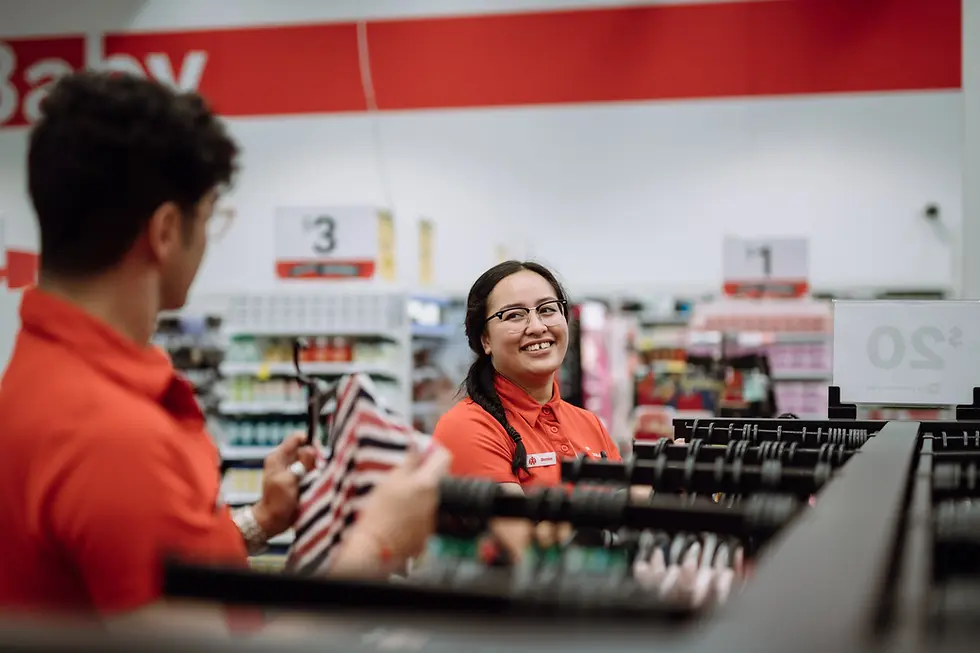 Two retail workers in red shirts, smiling and checking merchandise in store.