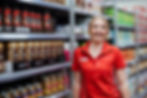 Smiling employee in red shirt stands by shelves with coffee products and careers.