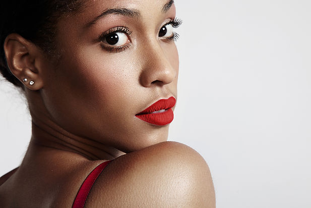 Elegant dark bronze woman with captivating gaze, showcasing the outcomes of a red carpet treatment received at an aesthetic clinic in London. Her smooth complexion highlights the effects of the procedure, while her striking red lipstick adds a touch of glamour to her overall look.