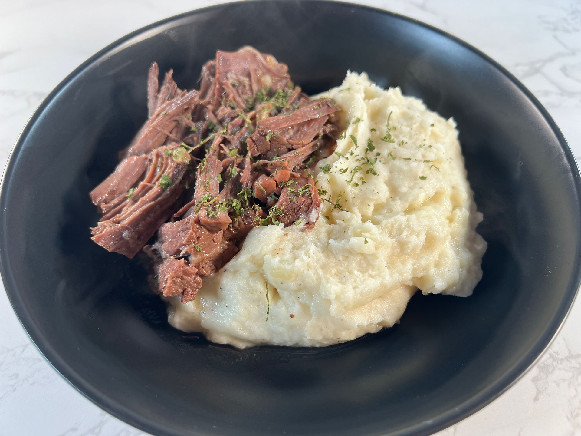 a bowl filled with shredded pot roast alongside creamy mashed potatoes