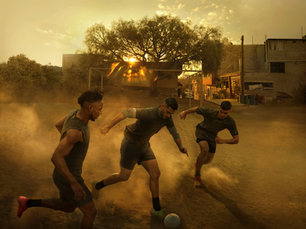 Fotografia de três jogadores em um campo de terra durante o pôr do sol, com luz quente e poeira no ambiente, parte de projeto de Annie Leibovitz sobre futebol para a Copa de 2026.