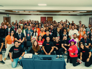 Grupo de fotógrafos reunidos em workshop presencial da Fotto, com participantes sorrindo e levantando as mãos durante encontro de educação, tecnologia e comunidade fotográfica.