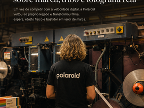 Pessoa de costas dentro de uma fábrica de filmes Polaroid, cercada por máquinas industriais, rolos de filme e caixas de fotografia instantânea, com título sobre marca, tribo e fotografia real.