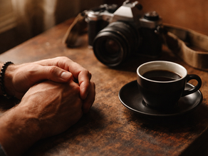 Mãos de fotógrafo sobre mesa de madeira com xícara de café, luz natural, tom editorial
