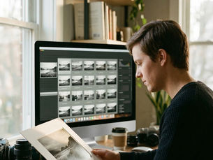 fotógrafo analisando fotografia impressa enquanto monitor mostra múltiplas variações digitais geradas por IA