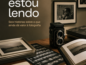 Mesa de trabalho com câmera fotográfica, fotolivros, provas de contato, fotografias impressas e anotações.