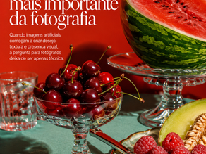 Natureza-morta ultra realista em formato vertical, com fundo vermelho intenso e mesa verde-água. À esquerda, o título em letras grandes brancas diz “A IA está mudando a pergunta mais importante da fotografia”, seguido de um subtítulo menor sobre imagens artificiais, desejo, textura e presença visual. À direita e na parte inferior, uma composição com frutas e objetos de vidro: meia melancia sobre pedestal de cristal, taça com cerejas vermelhas brilhantes, prato com framboesas, fatias de melão e talheres dourados, além de um copo de vidro e algumas cerejas soltas sobre a mesa. A imagem tem luz forte, sombras marcadas e estética editorial sofisticada.