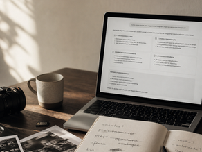 Mesa de trabalho de fotógrafo com laptop exibindo uma resposta de IA, caderno com anotações sobre clientes, preço e posicionamento, câmera, fotos impressas e xícara em luz natural.