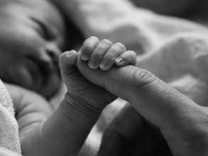 Recém-nascido segurando o dedo de um adulto, em preto e branco, no contexto do registro do nascimento