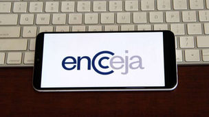 Logo do Encceja na tela de um celular apoiado sobre uma mesa de madeira escura.