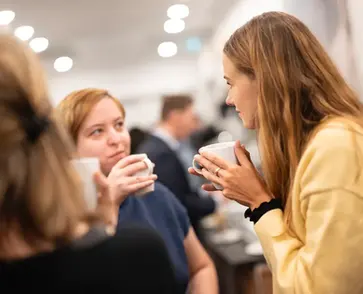 Teilnehmerinnen eines Seminars unterhalten sich in einer Kaffeepause in einem Konferenzzentrum.