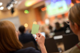 Auf einem Kongress hält eine Teilnehmerin eine grüne Karte für eine Abstimmung hoch.