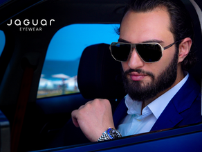 Óculos de grau masculino Jaguar Eyewear em titânio, com design aerodinâmico inspirado em carros de luxo, sobre superfície de couro preta dourada.