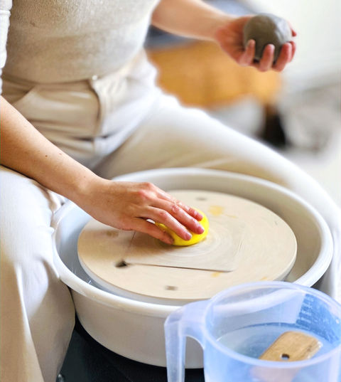 Potter sitting at the pottery wheel with a ball of clay in hand