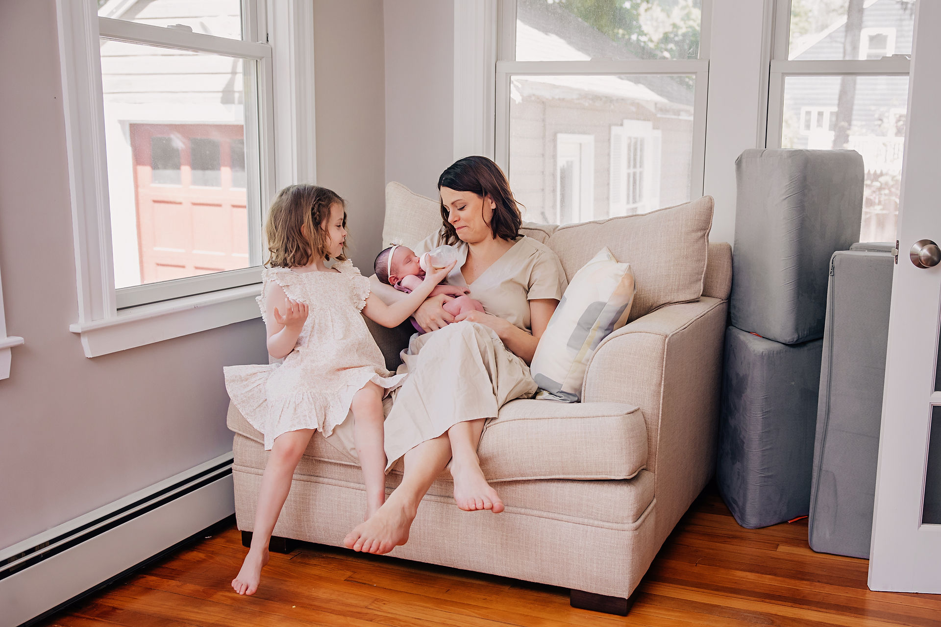 Mother feeding her newborn on a couch while sibling interacts during an in-home newborn session