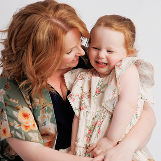 Mother cuddling and smiling with her young daughter during a soft, light-filled portrait session in a Boston photography studio.